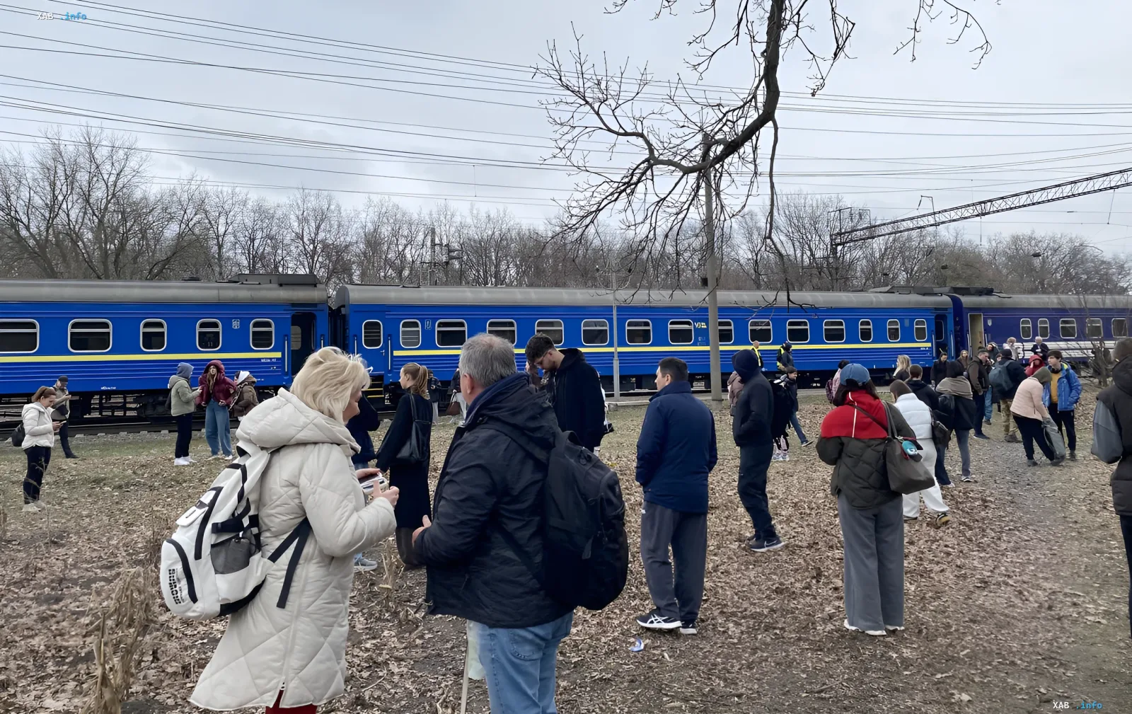 Evakuierte Passagiere des Zuges Odessa–Dnipro stehen auf freiem Gelände neben dem blauen Zug nach einem Drohnenschlag auf der Prydniprowaja-Bahnstrecke
