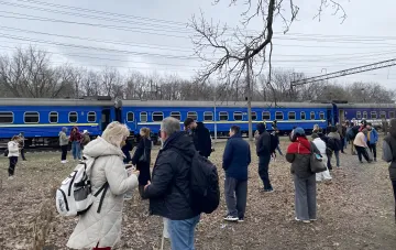 Evakuierte Passagiere des Zuges Odessa–Dnipro stehen auf freiem Gelände neben dem blauen Zug nach einem Drohnenschlag auf der Prydniprowaja-Bahnstrecke