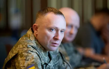 Командир ВСУ в цифровой форме с нашивкой украинского флага на фоне совещания — контекст «Принципов лидерства», где люди важнее техники