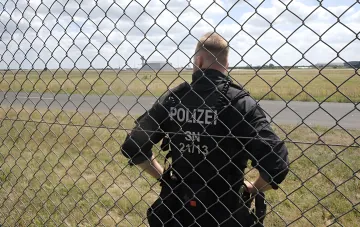 Немецкий полицейский за оградой на фоне аэродрома: усиление безопасности в Германии после атаки дрона в Лейпциге