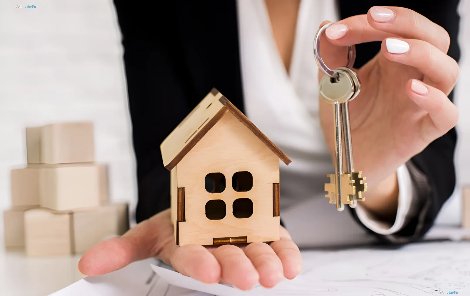 Frau hält ein Holzhaus-Modell und einen Schlüsselbund – Symbol für Wohnungsübergabe und steigende Immobilienpreise in der Ukraine