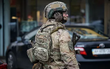Солдат в камуфляже с тактическим снаряжением на фоне киевских Берёзняков после стрельбы
