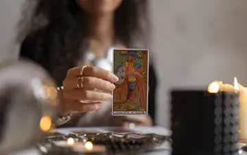 Tarot-Leserin hält die Karte Ritter der Stäbe bei Kerzenschein — Tarot-Prognose für September 2026 für Sternzeichen