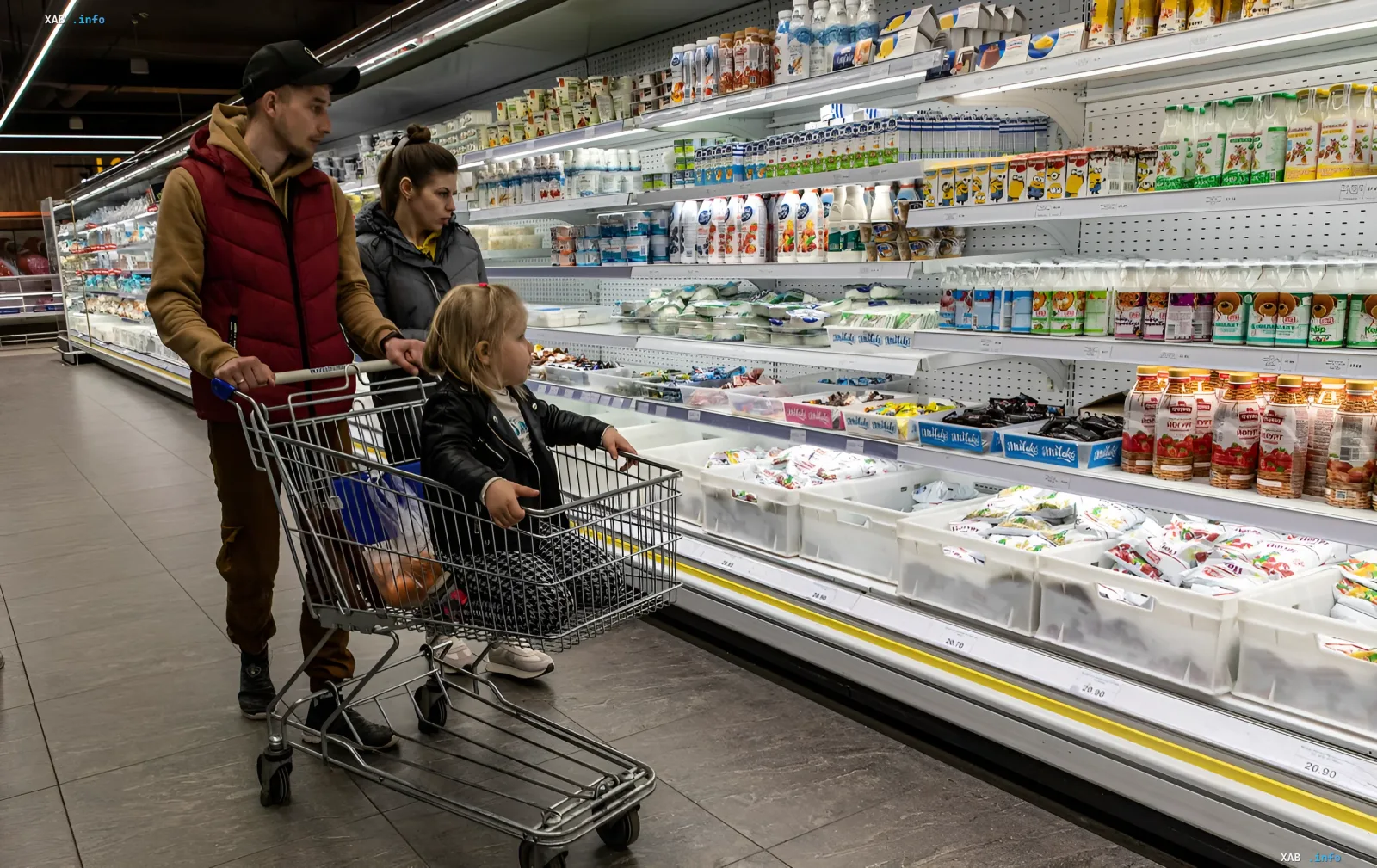 A family with a child in the shopping cart picks groceries at a supermarket in front of dairy and confectionery shelves amid discussion of food prices in Ukraine