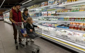 A family with a child in the shopping cart picks groceries at a supermarket in front of dairy and confectionery shelves amid discussion of food prices in Ukraine