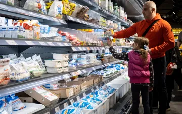Shoppers at refrigerated shelves with chilled dairy products in a supermarket amid rising prices