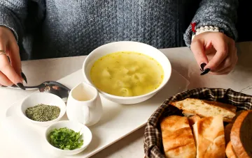 Пересоленный суп: как исправить вкус блюда по советам шеф-поваров — миска бульона со свежей зеленью, сушёными травами и нарезным хлебом