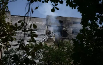 Feuerwehrmann auf einer Hebebühne löscht Rauch aus einem beschädigten Fenster eines Neunstockers nach einem Drohnenangriff im Kiwer Stadtteil Holosiwka