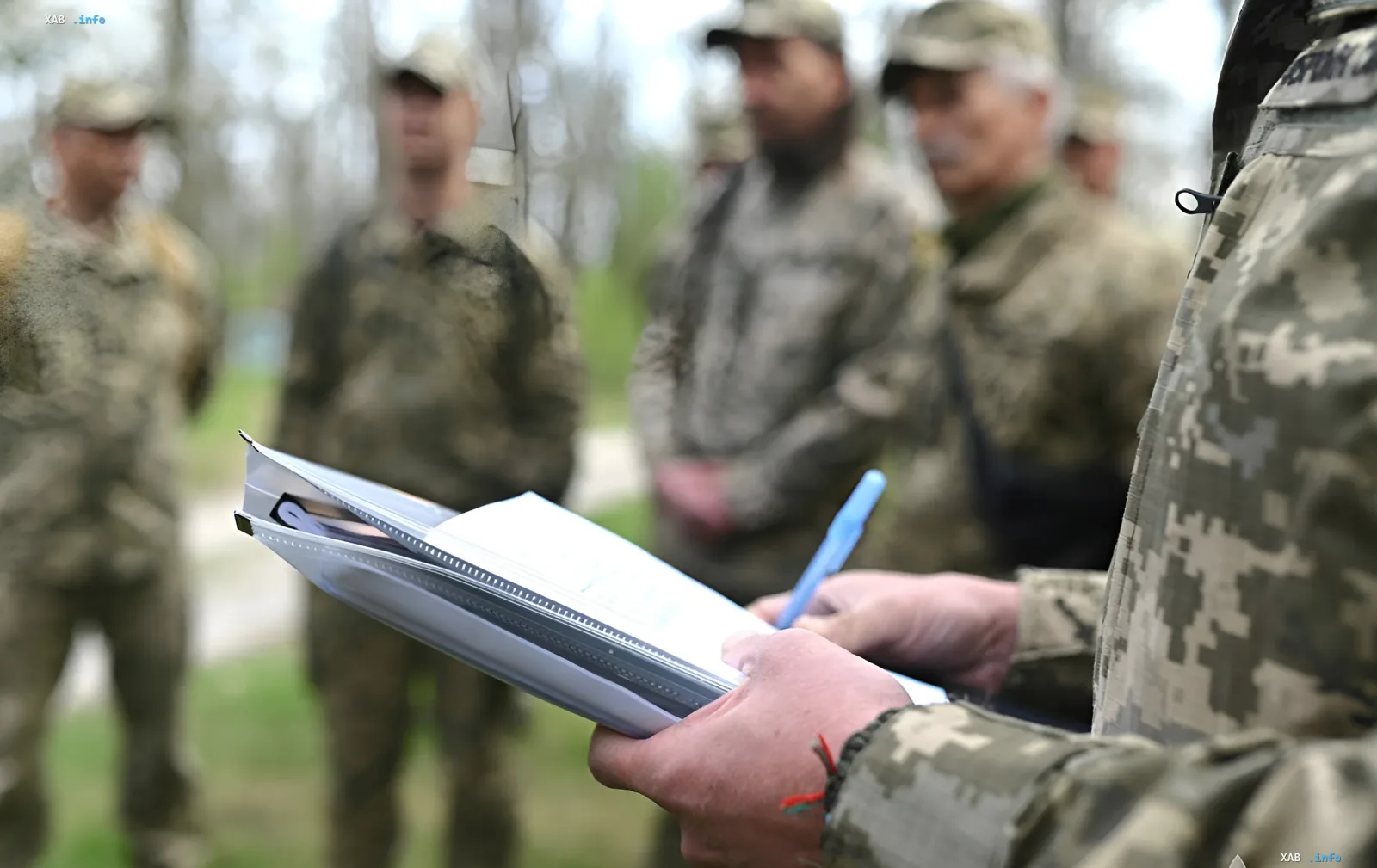 Dokumentenprüfung beim TCC: uniformierter Beamter mit Aktenordner und Stift, im Hintergrund eine Gruppe in militärischer Uniform — Fall der rechtswidrigen Festhaltung eines Arztes und Vaters von fünf Kindern in Kiew
