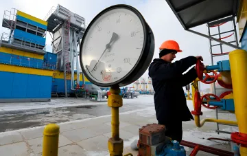 Оператор газового оборудования в каске управляет вентилем рядом с манометром на газовой станции в Украине