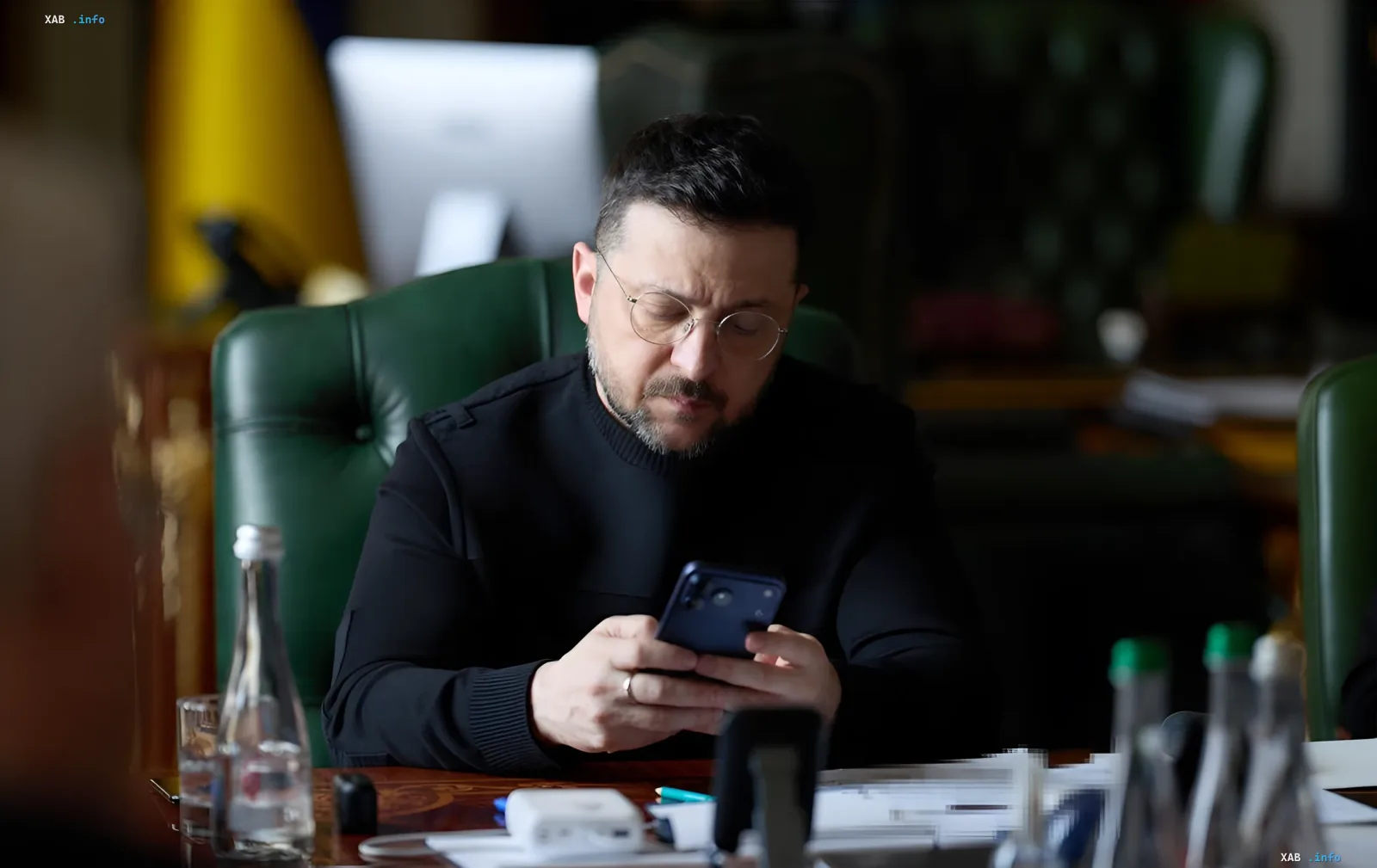 Владимир Зеленский за рабочим столом в кабинете, изучающий смартфон на фоне украинского флага — в контексте внесения в Раду законопроекта об уголовной ответственности за дроп и мошенничество с платежными инструментами