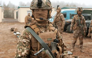 Kämpfer des 16. Armeekorps der ukrainischen Streitkräfte in Taktischer Ausrüstung und Gesichtsmaske vor militärischem Fahrzeug und Kameraden