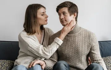 Пара на диване: женщина нежно касается щеки мужчины, иллюстрация знаков Зодиака, которые не могут отпустить бывших