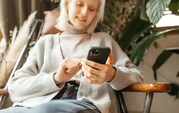 Женщина смотрит на iPhone с eSIM, иллюстрирующая функцию Handoff в iOS 27 для одного номера на двух смартфонах