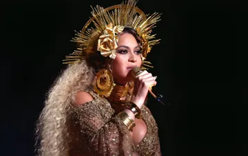 Beyoncé on stage in a golden crown and sparkling outfit, singing into a microphone