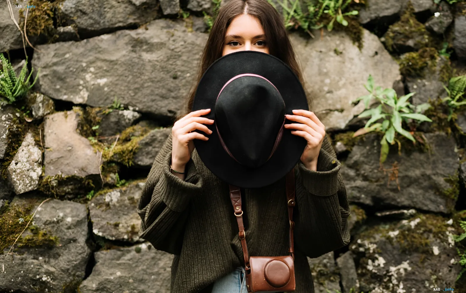 Woman holding a black hat in front of her face to demonstrate choosing a hat by face shape