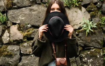 Woman holding a black hat in front of her face to demonstrate choosing a hat by face shape