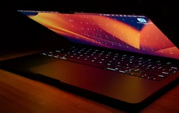 MacBook с ярким экраном в тёмном интерьере — устройство для macOS 27 Golden Gate с ИИ-ассистентом Siri