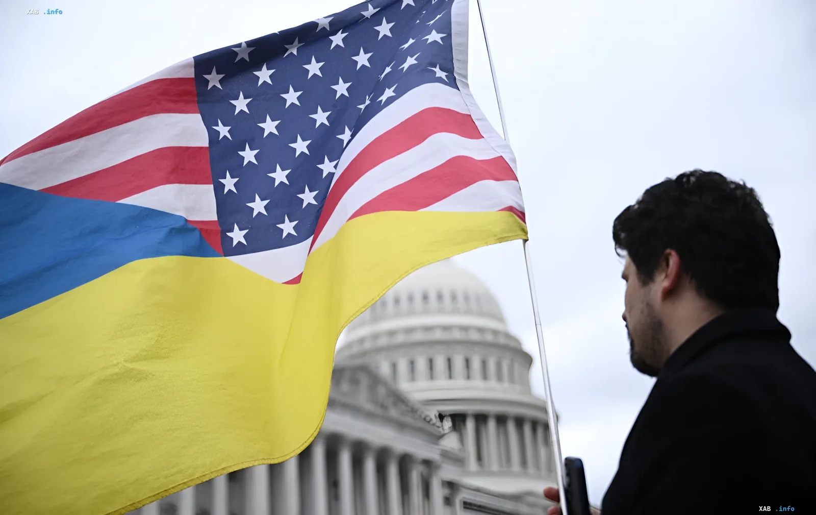 Мужчина держит флаги США и Украины на фоне купола Капитолия, где обсуждаются санкции против России