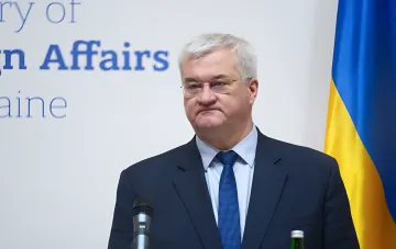 Представник МЗС України біля мікрофона на тлі прапора країни під час заяви про перенесення візитів делегацій