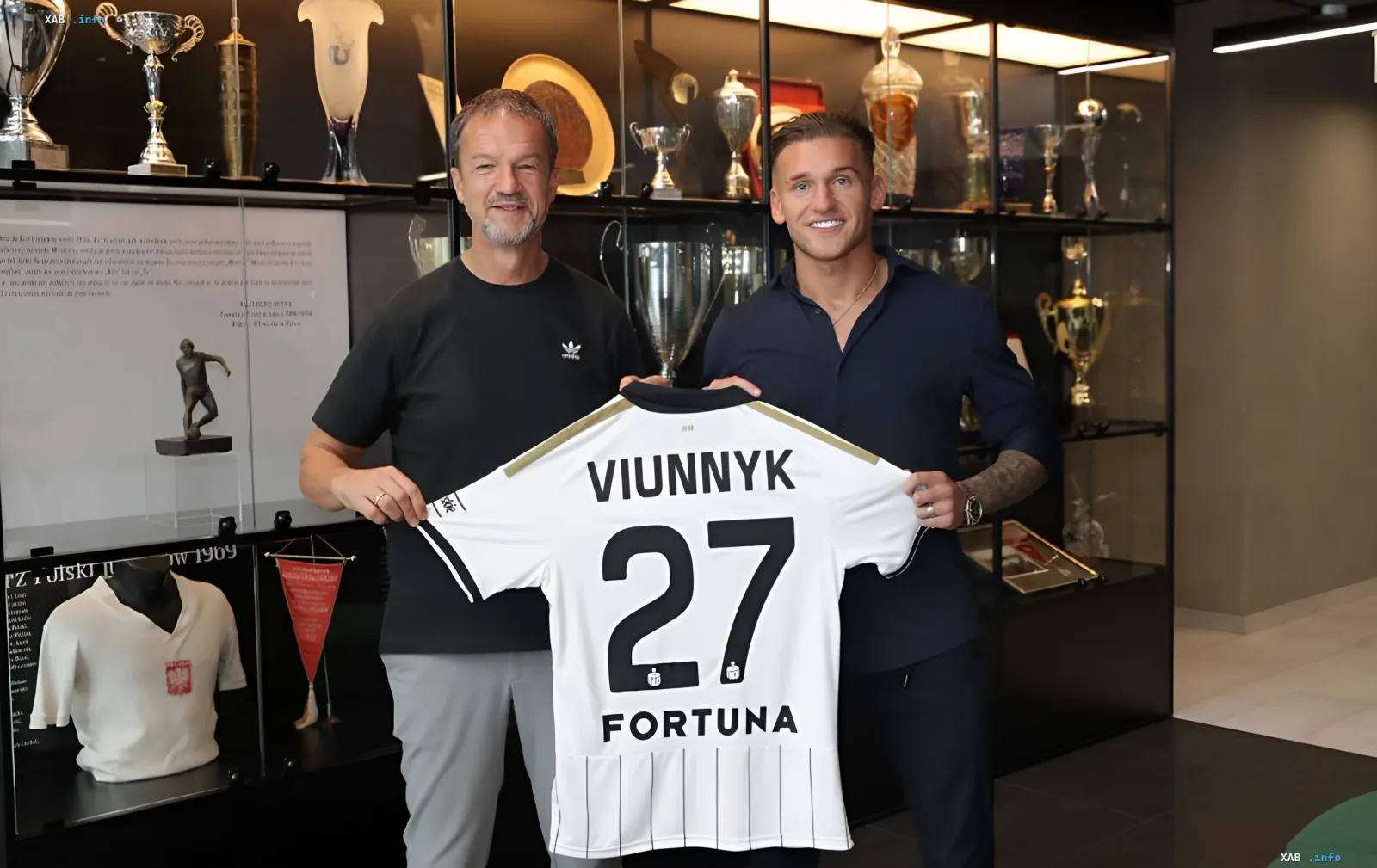 Bogdan Viunnyk and a Legia Warsaw representative hold a jersey with the name VIUNNYK and number 27 in front of the club museum
