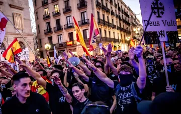 Ультраправые активисты в Мадриде на протесте против мигрантов демонстрируют нацистские жесты и несут флаги Испании и плакат с лозунгом Deus Vult