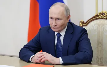 Vladimir Putin seated at a desk in an office with the Russian flag in the background — context of the GRU 'shadow war' against NATO and sabotage in Germany