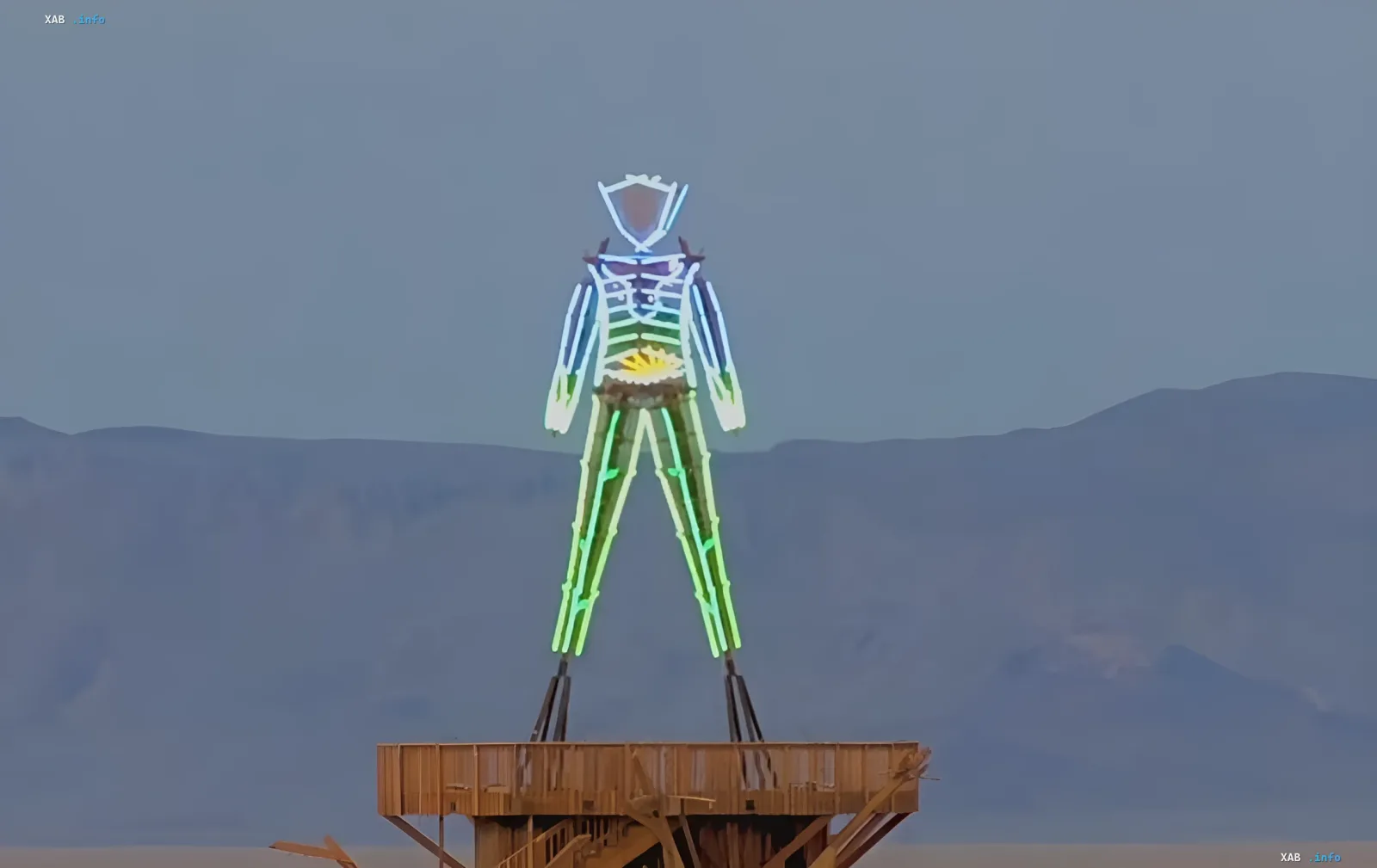 Leuchtende Neon-Figur eines Menschen auf einer Holzplattform — Kunstinstallation von Burning Man 2026 in der Nevada-Wüste