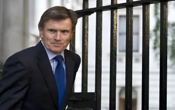 Экс-глава MI6 в деловом костюме у чёрной решётки, высказавший мнение о сроках мирных переговоров Украины и России