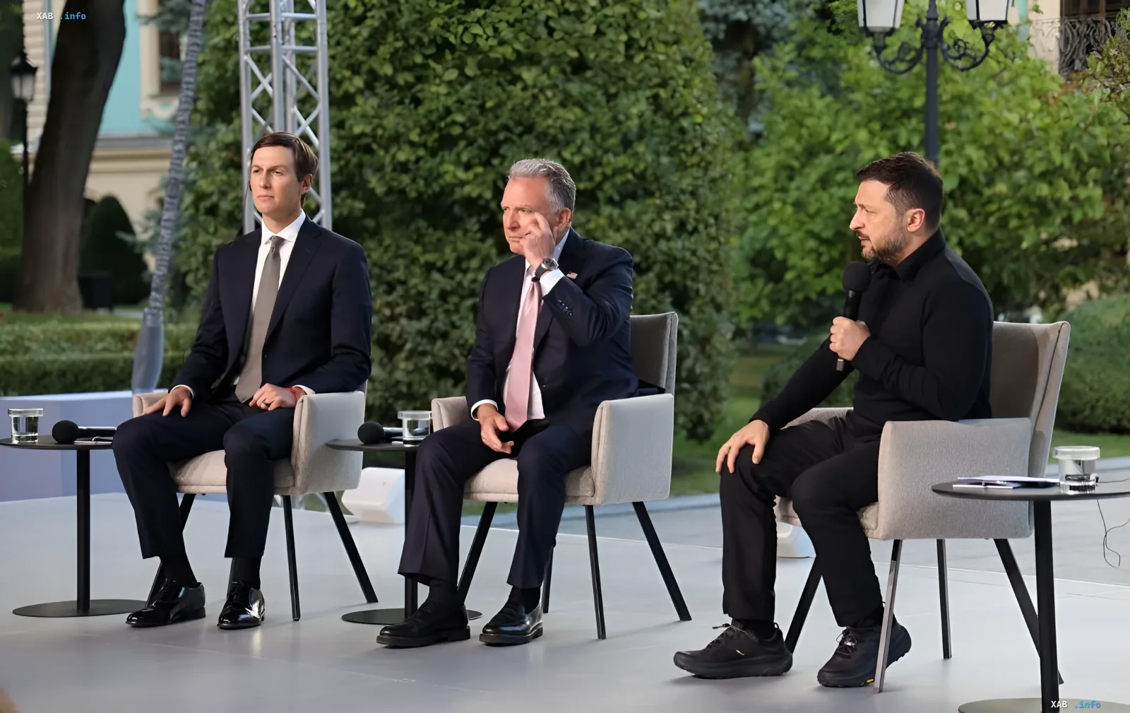 Zelensky in talks with Kushner and Witkoff in Kyiv: three men seated in chairs outdoors, Zelensky holding a microphone