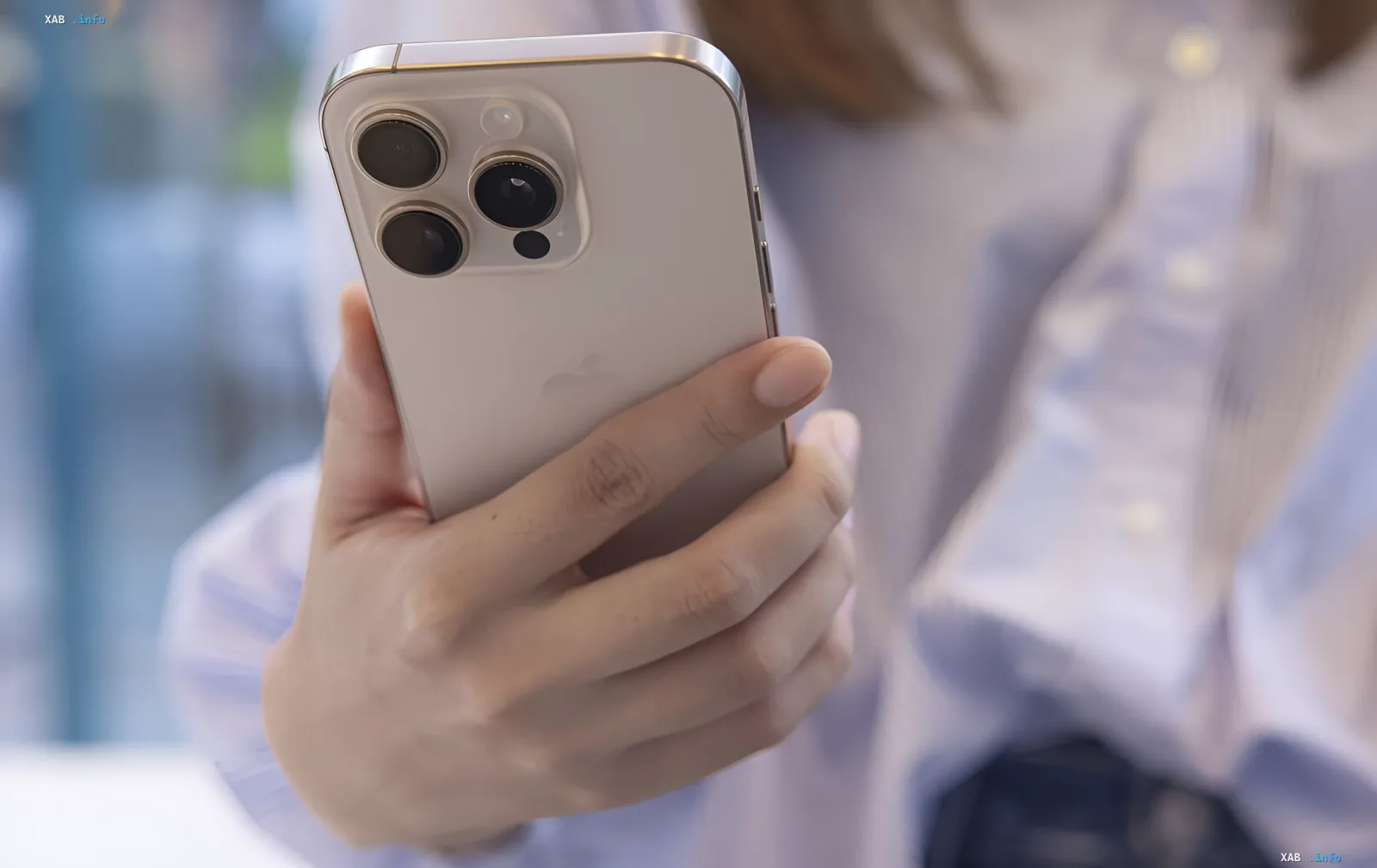 Человек держит официальный iPhone с тремя камерами на фоне размытого уличного пейзажа