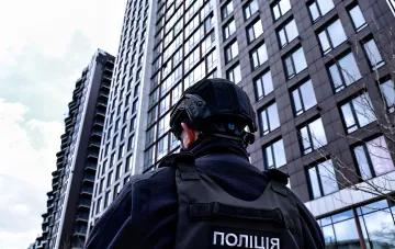 Полицейский в тактическом снаряжении и бронежилете с надписью ПОЛІЦІЯ на фоне многоэтажных зданий Киева — инцидент со стрельбой при задержании в Соломенском районе