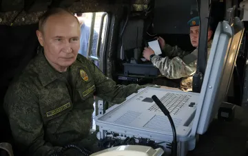 Wladimir Putin in Tarnung an einem militärischen Kommandogerät vor dem Hintergrund des Rekordverteidigungsbudgets Russlands