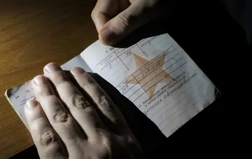 Hands holding an old military document with handwritten entries and a red star — illustration for the news on Russia's first travel ban for a reserve conscript ordered by the military commissariat