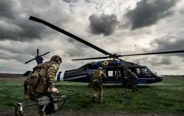Spezialkräfte des HUR in Taktischer Ausrüstung neben einem Militärhubschrauber unter stürmischem Himmel — Symbol der Militärgeheimdienste