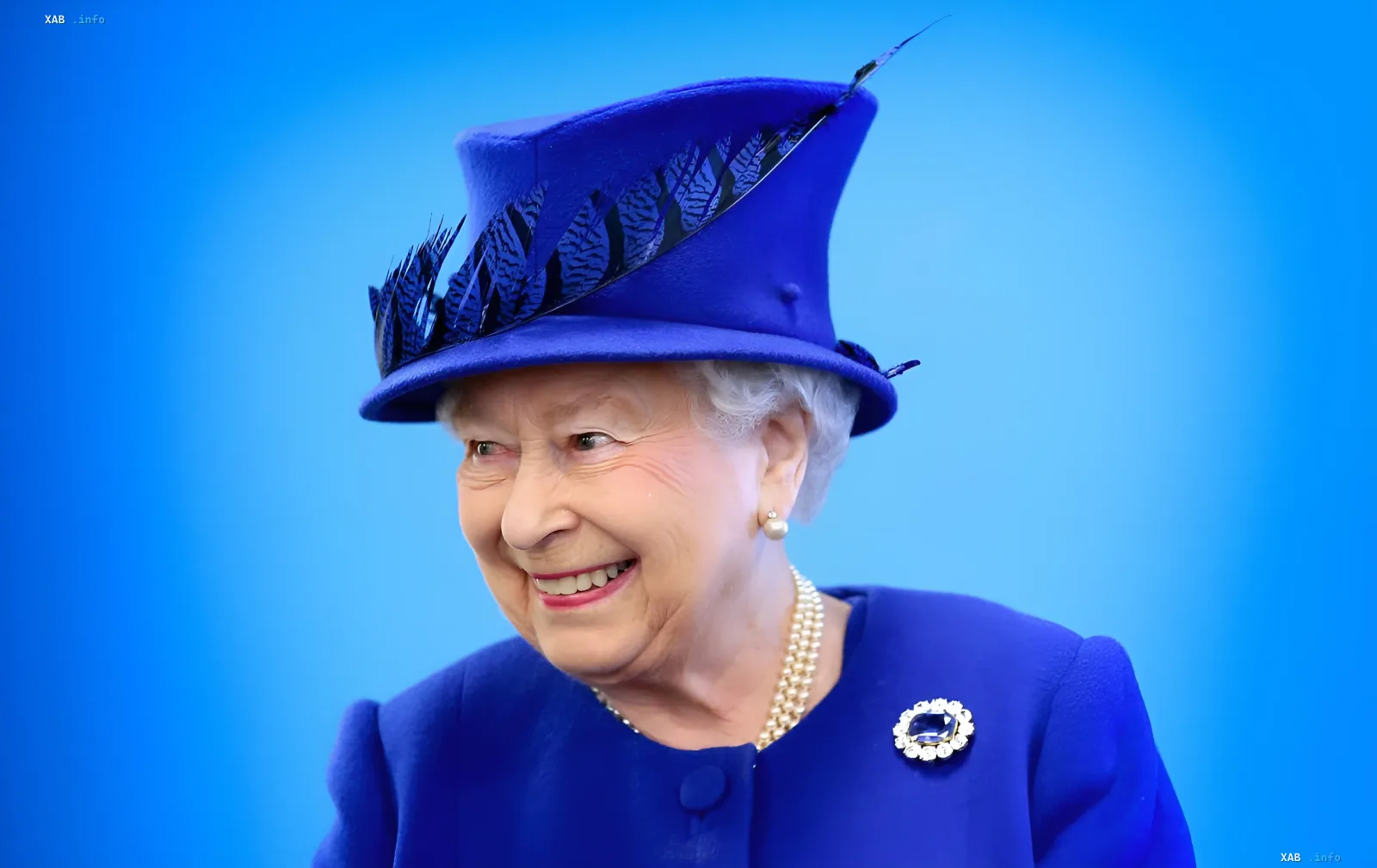 Königin Elisabeth II in einem leuchtend kobaltblauen Kostüm und Federhut — ein Beispiel dafür, wie ihre Outfits zur Sprache der Diplomatie wurden