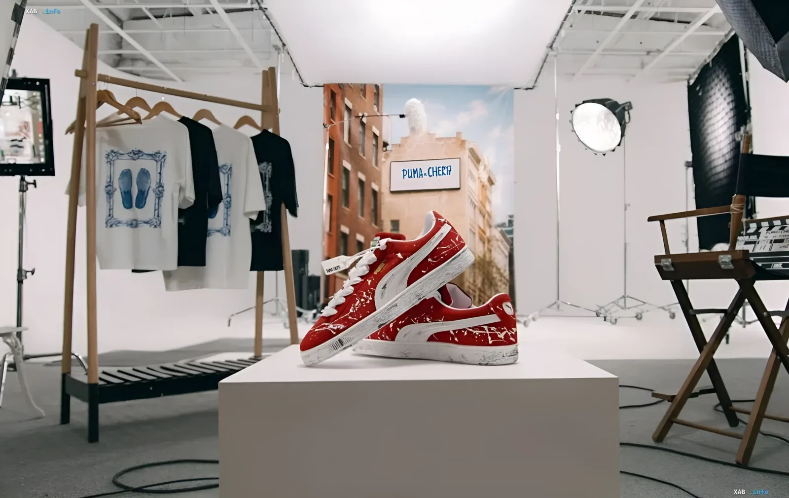 Красные кроссовки PUMA Suede с эффектом потертости и брызгами краски на подиуме в фотостудии, на фоне баннер PUMA x CHER'17 и вешалка с футболками коллекции