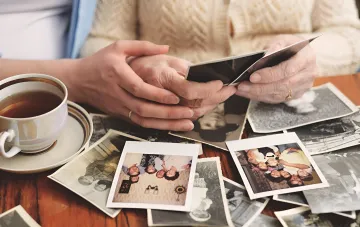 Hände zweier Generationen halten ein altes Familienfoto am Tisch neben einer Tasse Tee — Erinnerungen an ein Hochzeitsfoto aus dem Jahr 1926 aus Lwiw und die hundertjährige Geschichte einer Familie eines Maslosyuz-Kooperativen