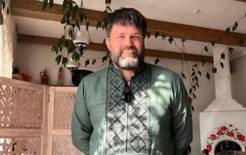 Magnus Carlsens Trainer in traditionellem Stickhemd vor einem Interieur mit Holzbalken und Volkskeramik — neues Mitglied des Vorstands des Ukrainischen Schachverbands
