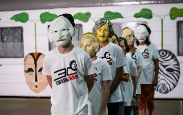 Участники перформанса «ГогольFest» в масках и футболках с логотипом «30 Гоголь Train» на фоне вагона с рисунками масок