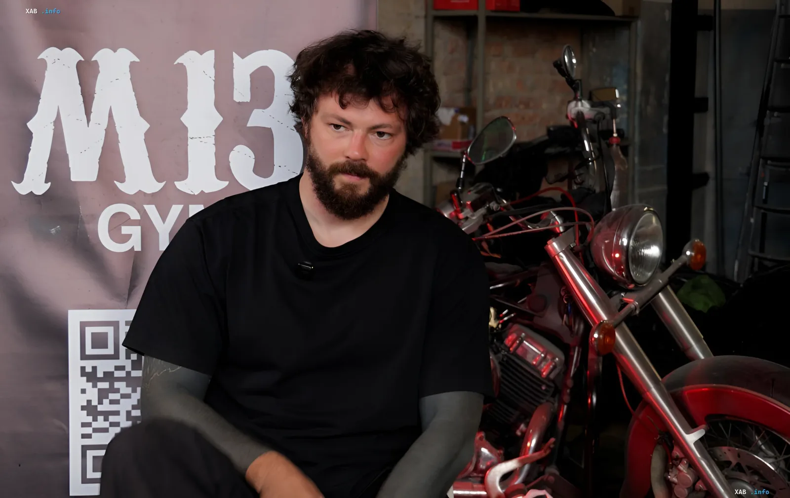 M13-Gründer Artem Hrot in schwarzem T-Shirt vor dem M13-Gym-Banner und einem Motorrad, der über Sport als Rehabilitation für Veteranen spricht