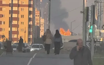Folgen eines Drohnenschlags: Rauch und Feuer vor beschädigten Gebäuden, während Anwohner die brennende Infrastruktur beobachten