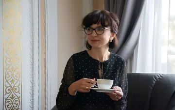 Елена Слободян, зарегистрированная ЦИК народной депутаткой, в очках и чёрном платье с белыми точками, держит чашку чая