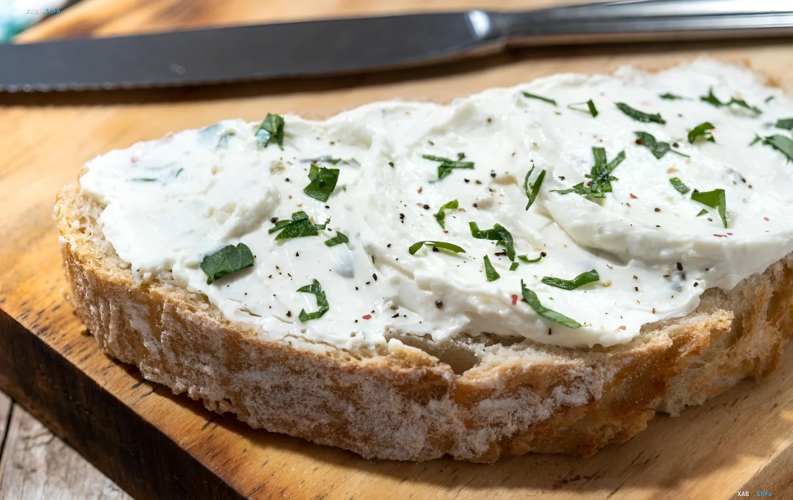 Cream cheese spread with roasted garlic on a slice of bread, topped with fresh herbs and pepper, on a wooden board
