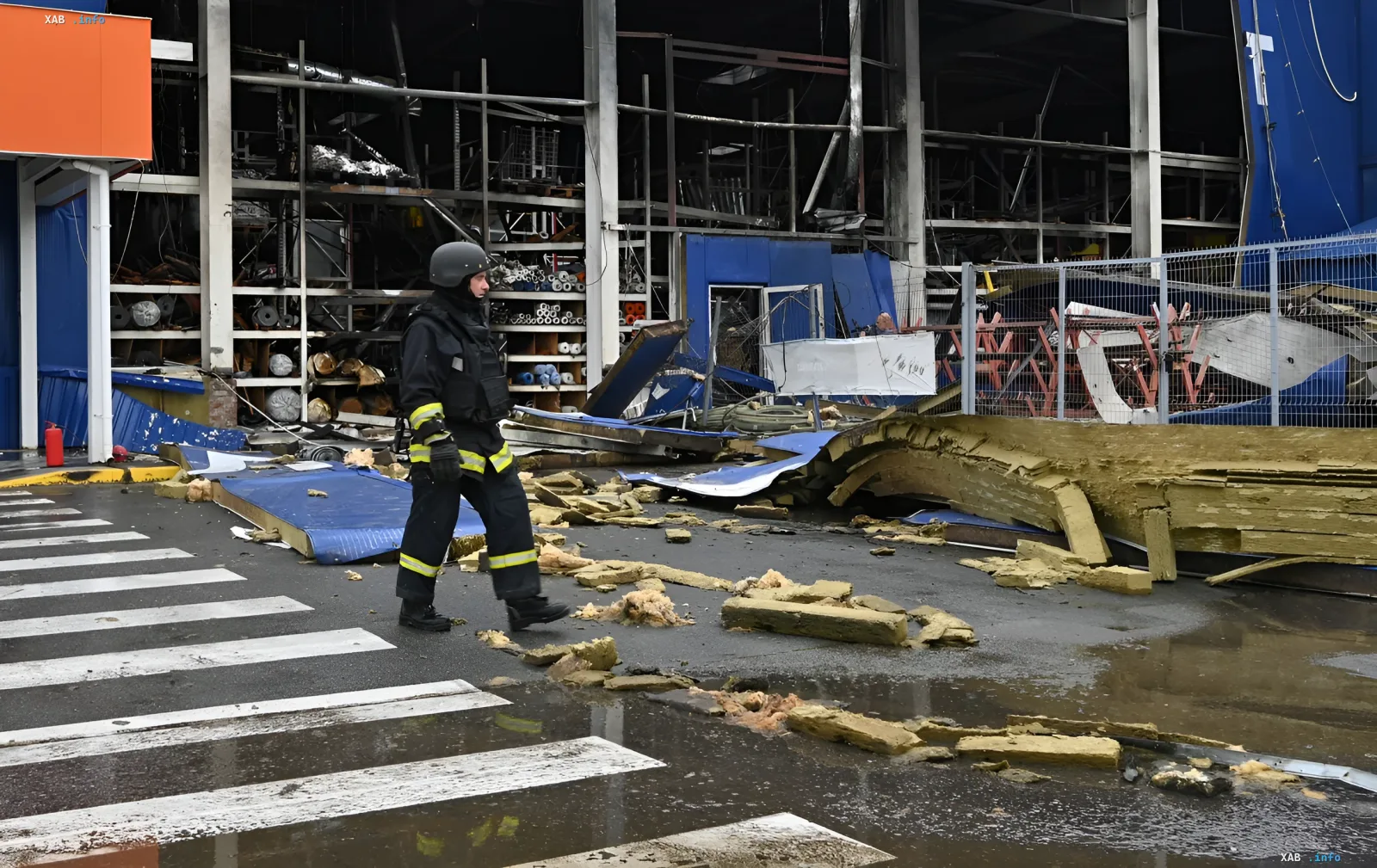 Damaged industrial facility after shelling: destroyed roof, debris, and military personnel in the background