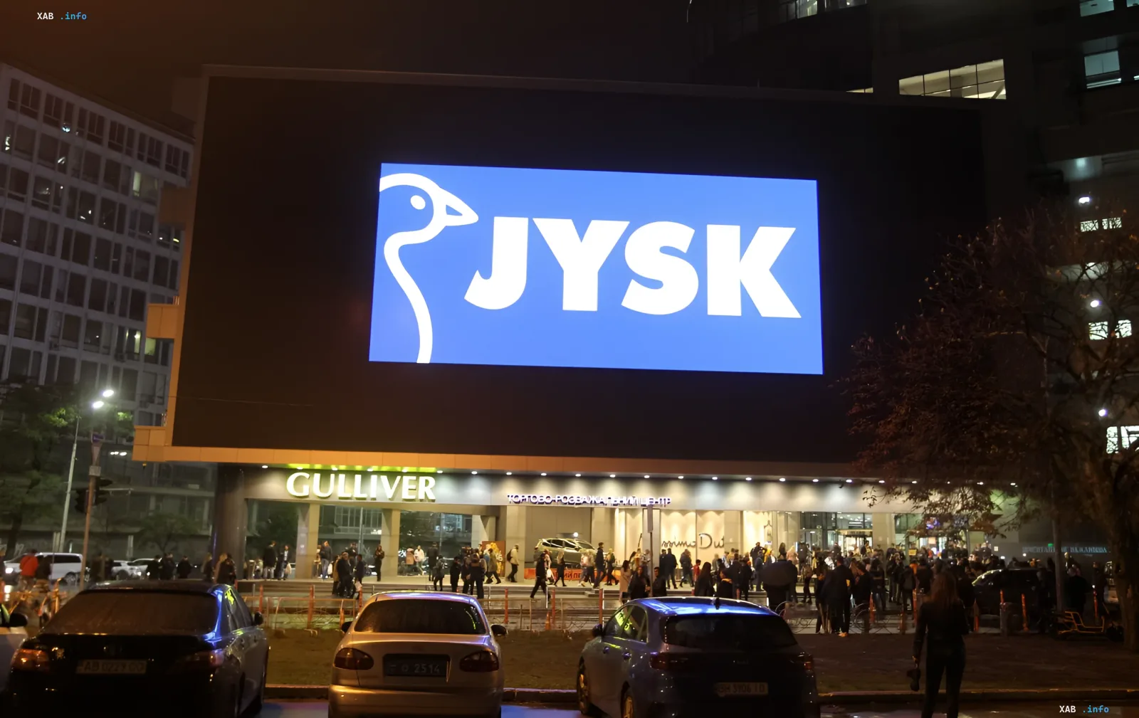 Nächtliche Fassade eines JYSK-Geschäfts in der Ukraine mit großem beleuchtetem Logo auf dem Bildschirm und einer Menschenmenge am Eingang, die Kette schließt Filialen bei jeder Luftalarmstufe