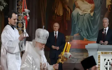 Church service scene: clergy in white vestments and laymen holding candles before the iconostasis, in the context of the ROC transferring relics of Dmitry Donskoy to the front in Ukraine