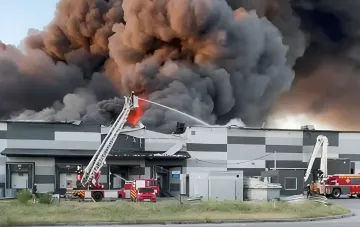 Fire at a VARUS warehouse in Dnipro after a strike: firefighters on aerial ladders fight the blaze as thick black smoke billows from the damaged roof