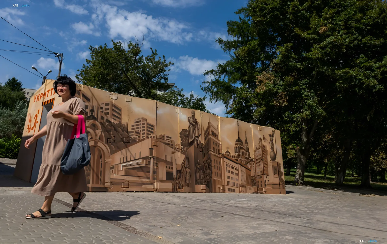 Woman walking past a mobile shelter with a mural of Kyiv landmarks in a Kyiv park
