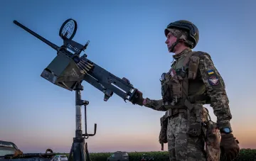 Ukrainian soldier at an anti-aircraft machine gun at dusk: air defense repels massive strike of over 410 Russian combat drones